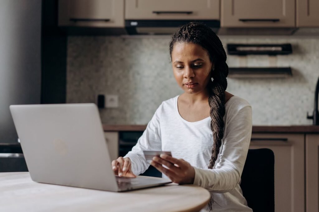 Shopper comparing products on a laptop with a payment card at home