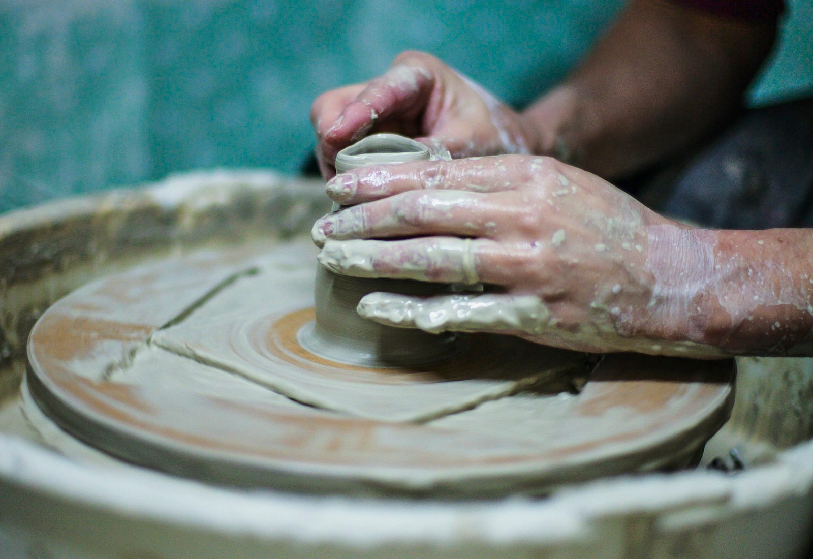 Hands shaping clay on a pottery wheel in a maker workshop