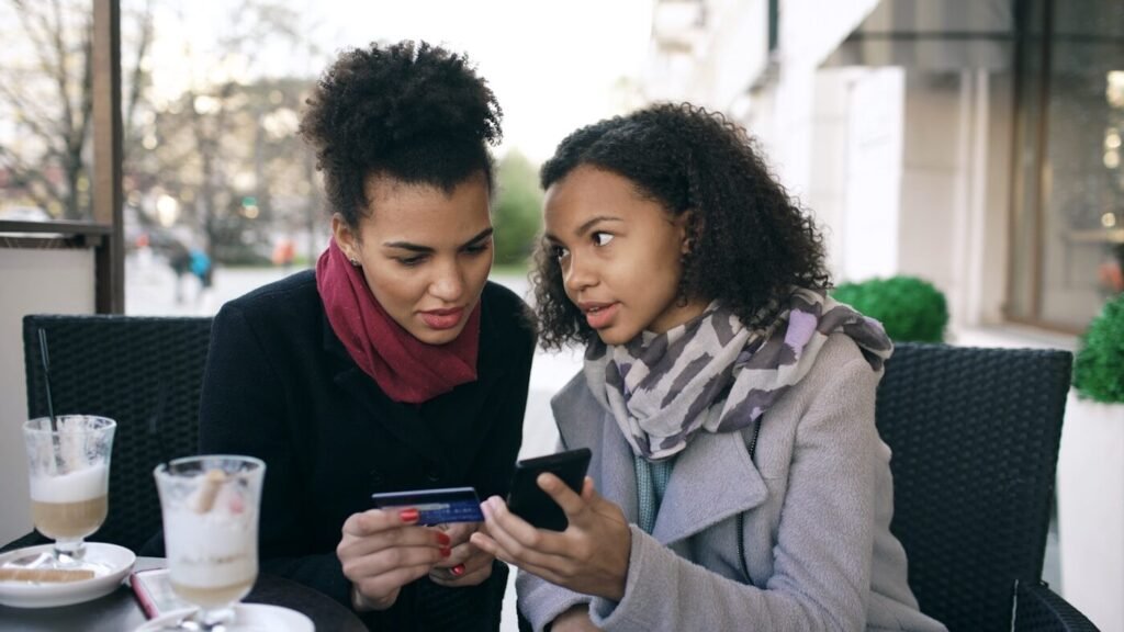Two shoppers comparing a fashion product on a phone with a payment card in hand