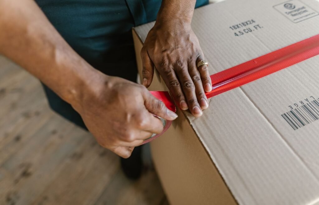 Hands taping a cardboard carton closed during prep before an inbound shipment to Amazon