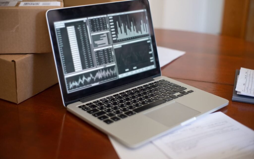 Laptop showing performance graphs beside stacked cardboard boxes in a small eCommerce office