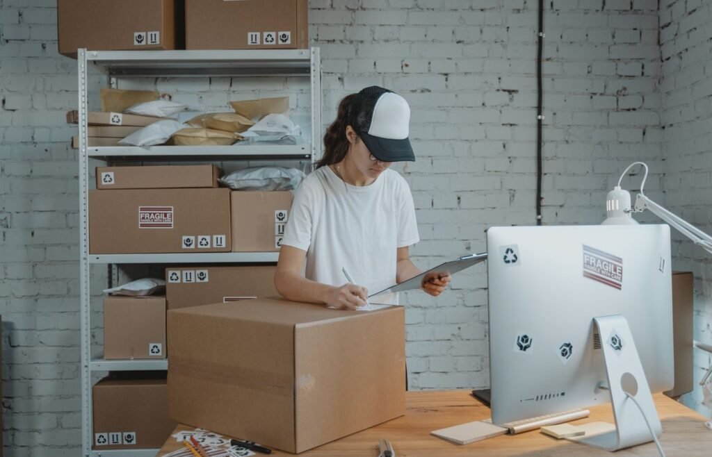 Operations worker checking catalogue details against a clipboard beside packed cartons