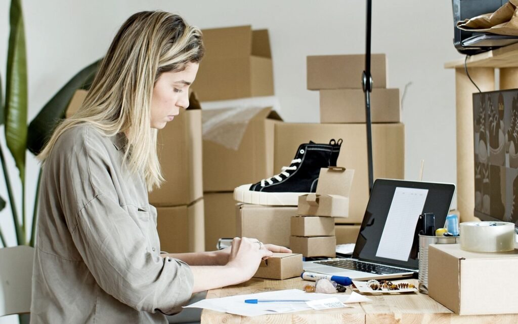 Store owner packing repeat customer orders beside a laptop in a small eCommerce workspace