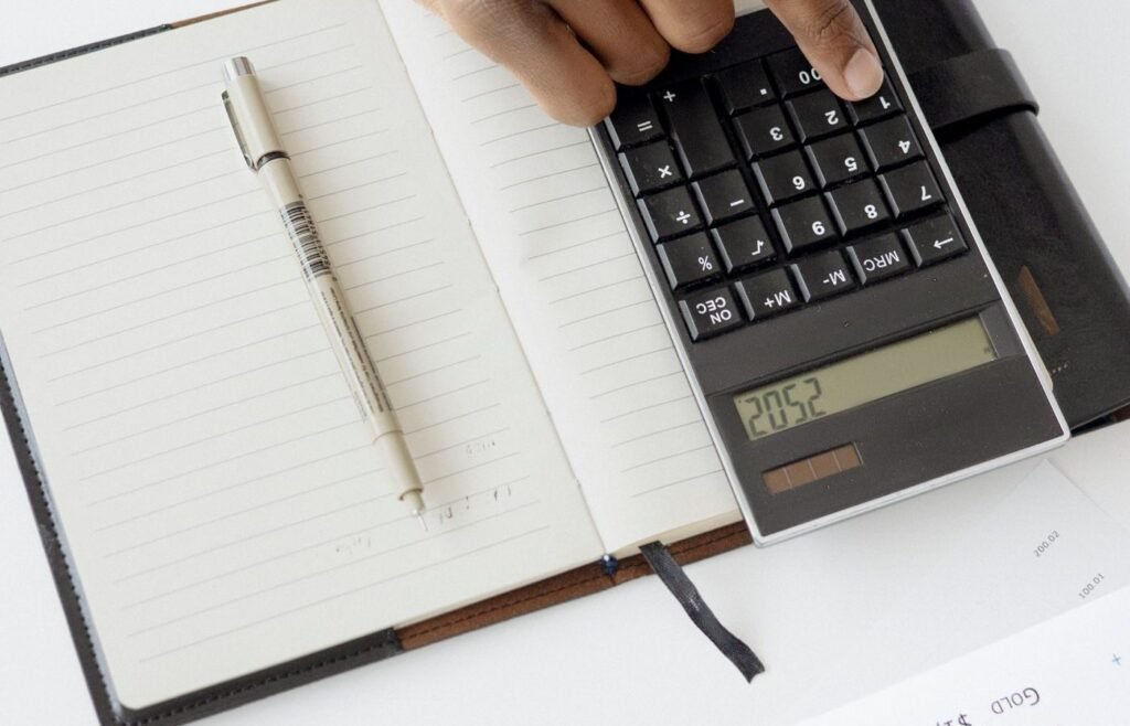 Hand working through cost lines with a calculator and notebook to find contribution per order